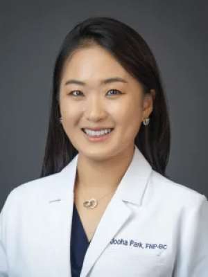 Smiling clinician in a white coat against a neutral gray background