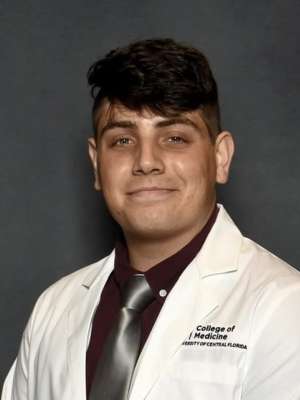Man wearing a white lab coat and tie on a gray backdrop.