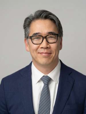 Professional headshot of smiling man wearing glasses, navy suit and tie.