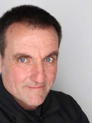 Man with short dark hair and blue eyes smiling slightly