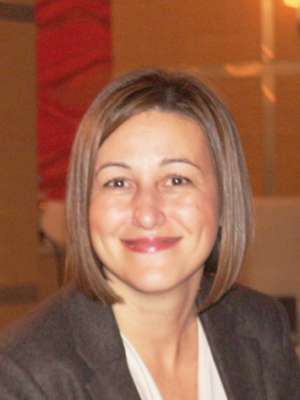 Person with short blonde hair wearing a gray blazer indoors