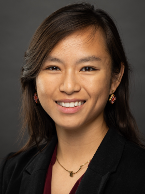 Smiling woman in blazer and necklace against a gray backdrop