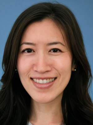 Smiling woman with dark hair, headshot on blue background.