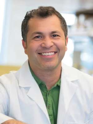 Dr. Hector Aguilar-Carreno sits wearing a lab coat and smiling