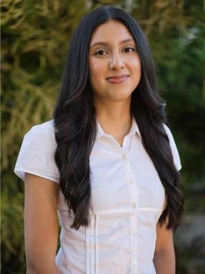 A woman with long, wavy hair wearing a white shirt, standing outdoors