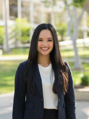 A headshot of Rejah Marie Nabong, a woman with long dark hair, smiling and wearing a dark blazer over a white top