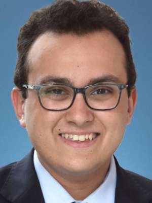 Smiling man with glasses in suit and tie against a blue background