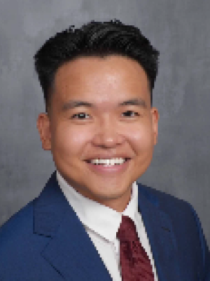 Headshot: smiling person in blue suit and red tie on gray backdrop