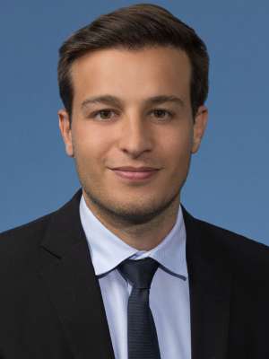 Man in dark suit and tie against blue background.