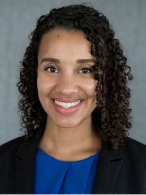 Professional headshot of a person with curly hair, wearing a blue top and black blazer.