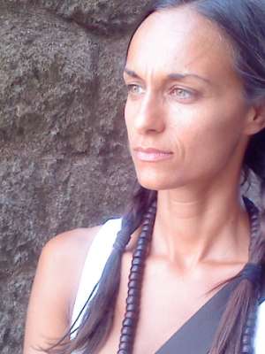 A young woman with braided hair stands against a stone wall.