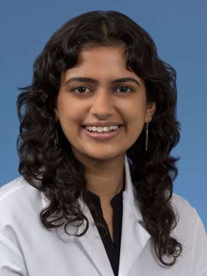 Head shot of Anjali Upadyaya in a white coat, smiling at the camera