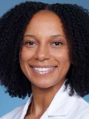 Smiling person wearing a white coat against a blue background.