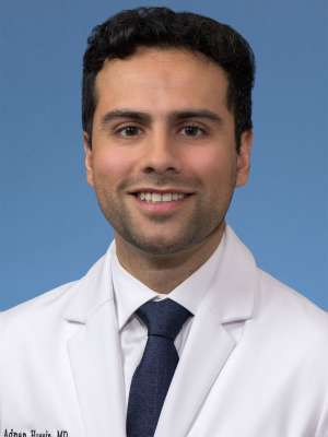 Head shot of Adnan Husein in white lab coat, smiling at camera