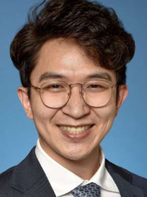 Smiling man with glasses in suit and tie against blue backdrop.