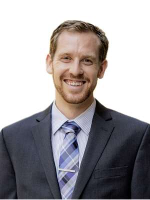 Smiling man in dark suit and striped tie, headshot on white background