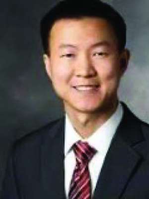 Smiling man in dark suit and striped tie against a neutral gray background