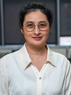 Headshot of Doctor Li wearing glasses and a white blouse, the background is blurry