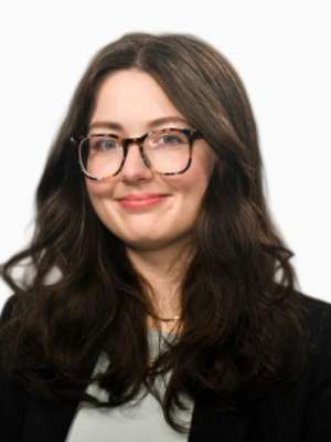 Woman with glasses and dark wavy hair in blazer smiling on white background