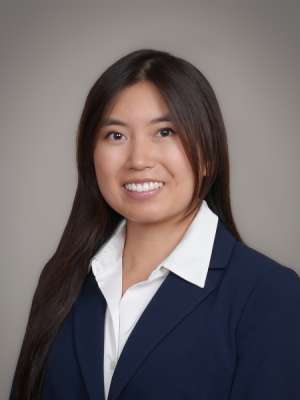 Smiling professional woman in navy blazer and white blouse, neutral studio background.