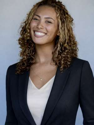 Smiling woman in navy blazer and white blouse against neutral gray background