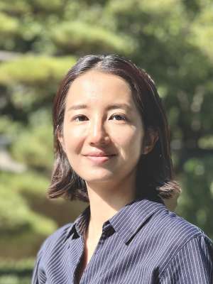 Woman with shoulder-length hair wearing a dark striped shirt, outdoors in a park.