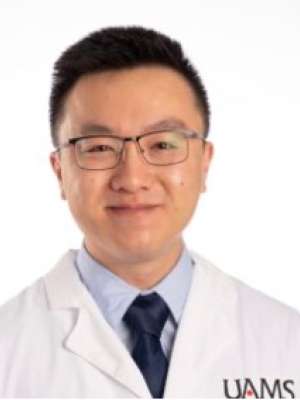 Smiling healthcare professional in UAMS white coat, tie, glasses