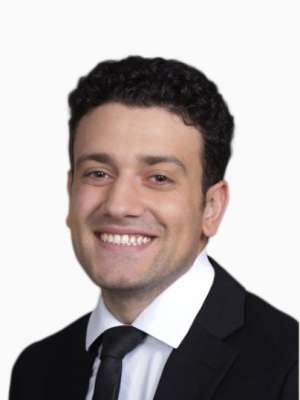 Headshot of smiling man in black suit and tie on white background.