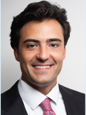 Smiling man in dark suit and pink tie on light background.
