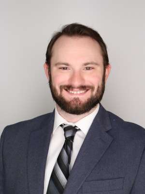 Professional headshot of smiling man in navy suit and striped tie