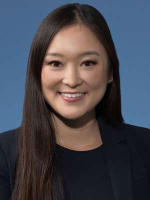 Smiling professional headshot of woman in blazer on blue background.