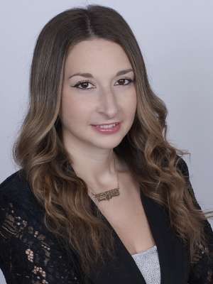 Headshot of Francesca Kimelman with wavy brown hair, black lace jacket, and gold nameplate necklace.