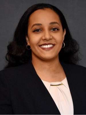 Bethlehem Michael professional headshot. Beth is smiling and wearing a black suit with light pink shirt. 