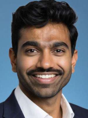 Smiling man wearing a suit and white shirt against blue background.