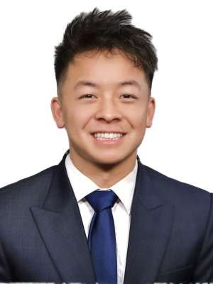 Smiling person in dark suit and tie against plain white background