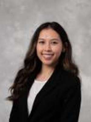 Professional headshot of woman in black blazer and white top against gray backdrop
