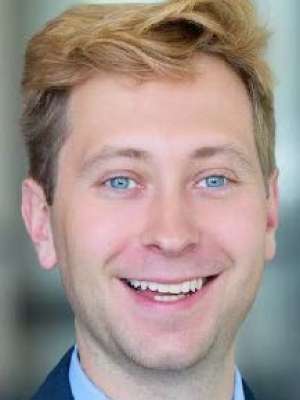 John Finlay with light hair smiling in a headshot against a blurred background, showing a friendly and approachable demeanor.