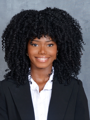 Headshot of smiling person with voluminous curly hair wearing a black blazer.