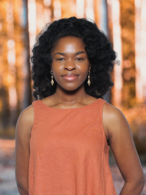 Woman in orange sleeveless top smiling against blurred autumn forest background