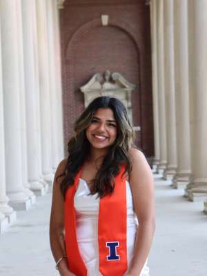 Smiling graduate wearing orange stole standing between classical stone columns