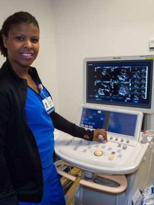 Woman in blue medical scrubs smiling while operating an ultrasound machine.