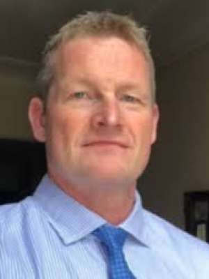 Headshot of man wearing blue shirt and tie against neutral background