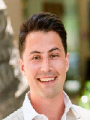 Smiling man in white shirt headshot against a blurred outdoor background