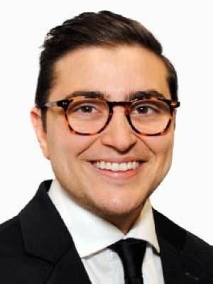 Caleb Bercu, smiling headshot, wearing suit, tie, and glasses