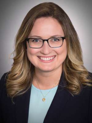 Emily Brown, smiling with glasses wearing blazer and necklace