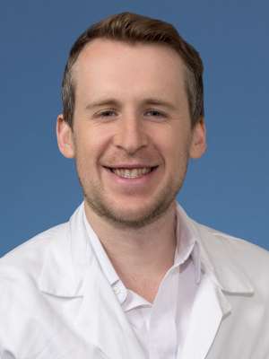 Smiling person in white lab coat and collared shirt on blue background