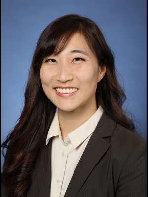 A woman with black hair, wearing a white collared shirt with a blazeer