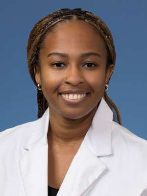 Head shot of Angela Udongwo, MD, MPH, in white coat, smiling at camera