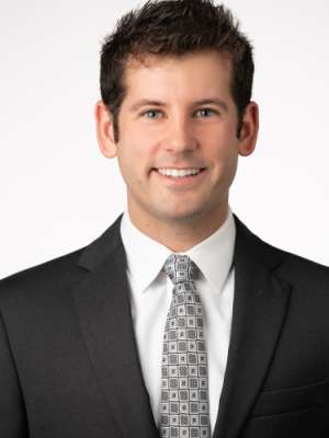 Headshot of person in black suit and patterned tie