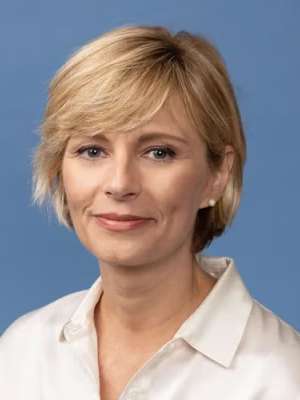 headshot of person with short blonde hair on a blue background.